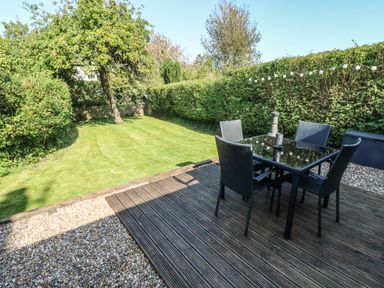 A garden with a wooden deck and glass table with four chairs at Oysterbank Cottage in Llangwm Pembrokeshire