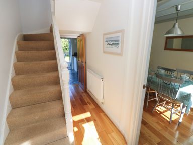 A hallway with carpeted stairs and wooden floor leading to an open door and a dining room with a table set with plates and glasses at Oysterbank Cottage in Llangwm Pembrokeshire