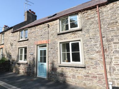Stone cottage with blue door and multiple windows on a street at Oysterbank Cottage in Llangwm Pembrokeshire