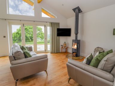 A living room with two sofas a wood burning stove a wall mounted television and large windows at Pen Bryn in Cyffylliog near Ruthin