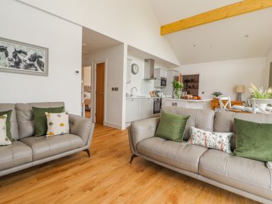 A living room with two grey sofas and green pillows looking towards a kitchen and dining area at Pen Bryn in Cyffylliog near Ruthin