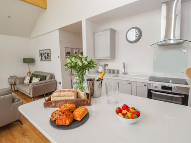 A kitchen with bread and pastries on the counter a bowl of fruit and a vase with flowers at Pen Bryn in Cyffylliog near Ruthin
