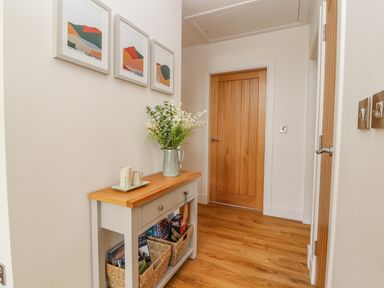 A hallway with a wooden console table with baskets and a vase with flowers near wooden doors at Pen Bryn in Cyffylliog near Ruthin