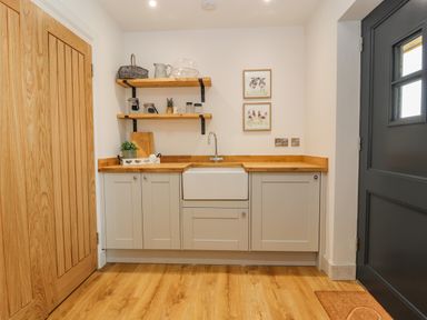 A kitchen with wooden countertops white cabinets a farmhouse sink and shelves with jars and decor at Pen Bryn in Cyffylliog near Ruthin