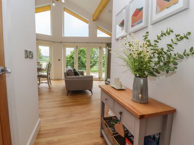 A hallway with a wooden console table holding a vase of flowers leading to a living room with sofas and large windows at Pen Bryn in Cyffylliog near Ruthin