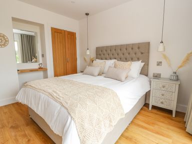 A bedroom with a double bed with pillows and a blanket beside a nightstand and wooden doors at Pen Bryn in Cyffylliog near Ruthin