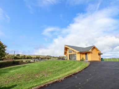 A wooden house with large windows on a grassy hill under a blue sky at Pen Bryn in Cyffylliog near Ruthin