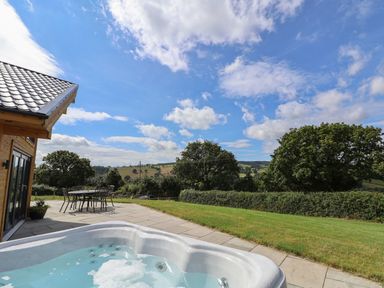 An outdoor patio with a hot tub and metal table and chairs overlooking a grassy yard and trees at Pen Bryn in Cyffylliog near Ruthin