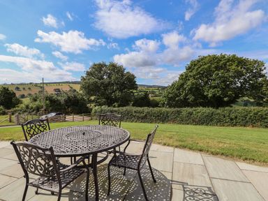 A metal outdoor table with four chairs on a stone patio overlooking trees and fields at Pen Bryn in Cyffylliog near Ruthin