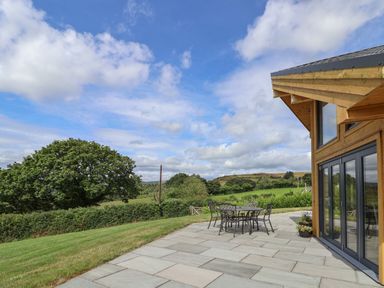 An outdoor patio with metal table and chairs next to a wooden house with glass doors and windows at Pen Bryn in Cyffylliog near Ruthin