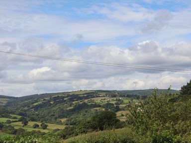 A landscape with hills trees and wind turbines under a cloudy sky at Pen Bryn in Cyffylliog near Ruthin