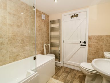 A bathroom with a bathtub a toilet a sink a chair and a white wooden door at Claire Cottage Gateforth near Hambleton North Yorkshire