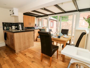 A kitchen and dining area with wooden floor a table set with dishes four chairs a high chair and glass doors leading outside at Claire Cottage in Gateforth near Hambleton North Yorkshire