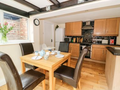 A kitchen with wooden cabinets a dining table with chairs and a window with flowers at Claire Cottage in Gateforth near Hambleton North Yorkshire
