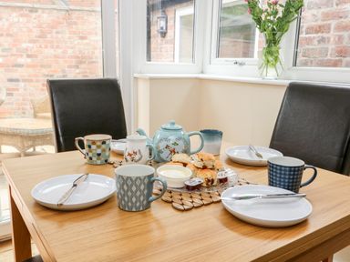 A dining table set with plates cups a teapot scones and jam in a room with windows and black chairs at Claire Cottage in Gateforth near Hambleton North Yorkshire