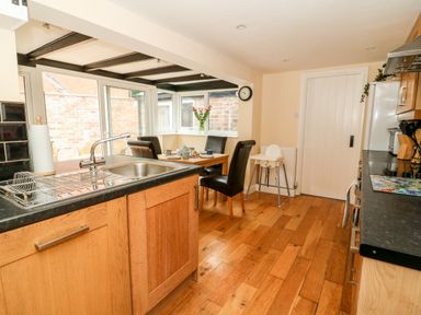A kitchen with wooden cabinets a sink and a dining table with black chairs at Claire Cottage in Gateforth near Hambleton North Yorkshire