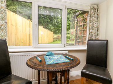 A small round wooden table with a scrabble board game set up between two black leather chairs by a window with curtains at Claire Cottage in Gateforth near Hambleton North Yorkshire