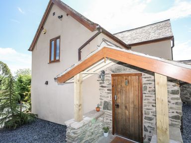 The exterior of a house with a wooden door set in a stone wall and a small porch roof supported by wooden beams at Hafotty Gelynen in Maerdy near Corwen