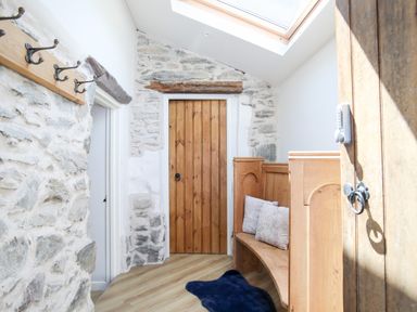 A hallway with stone walls wooden doors a wooden bench with cushions a coat rack and a skylight at Hafotty Gelynen in Maerdy near Corwen