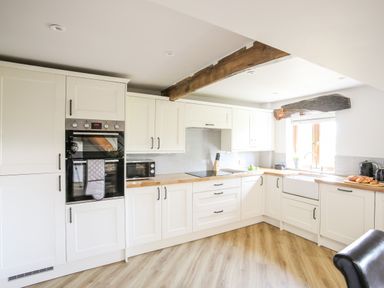 A kitchen with white cabinets wooden countertops an oven microwave a sink and a window with wooden beams at Hafotty Gelynen Maerdy near Corwen