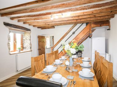 A dining room with a wooden table set with white dishes and glasses under exposed wooden beams at Hafotty Gelynen Maerdy near Corwen