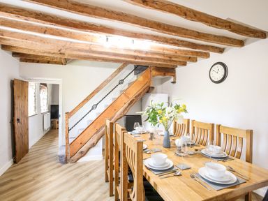 A dining room with wooden table and chairs set with plates and glasses under wooden ceiling beams at Hafotty Gelynen Maerdy near Corwen