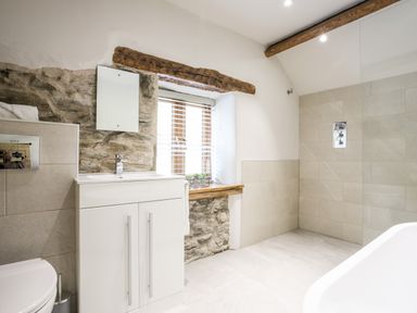 A bathroom with a white sink cabinet, stone wall sections, wooden window frame, and tiled walls at Hafotty Gelynen in Maerdy near Corwen