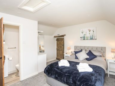 A bedroom with a bed covered in gray and blue bedding two folded towels on the bed two bedside tables with lamps a wooden door and an open door to a bathroom at Hafotty Gelynen in Maerdy near Corwen