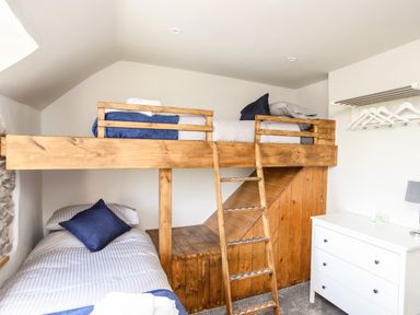 A bedroom with wooden bunk beds a white chest of drawers and a wall-mounted clothes rack with hangers at Hafotty Gelynen Maerdy near Corwen