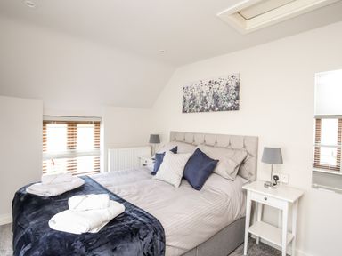 A bedroom with a double bed pillows and towels on the bed bedside tables lamps a window with blinds and wall art at Hafotty Gelynen Maerdy near Corwen