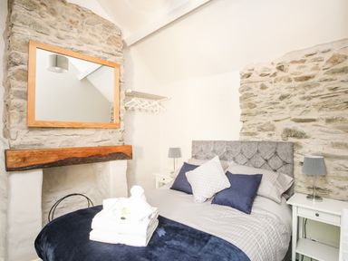 A bedroom with a double bed pillows bedside tables lamps a mirror and exposed stone walls at Hafotty Gelynen Maerdy near Corwen