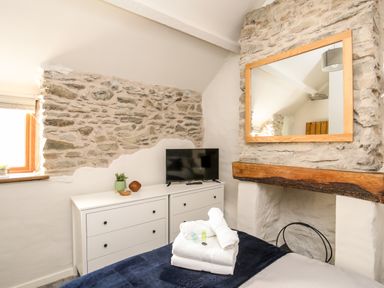 A bedroom with stone walls a dresser with a TV and a mirror above a fireplace at Hafotty Gelynen in Maerdy near Corwen