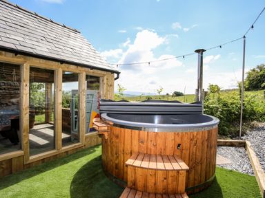 An outdoor wooden hot tub next to a wooden building with large windows at Hafotty Gelynen in Maerdy near Corwen