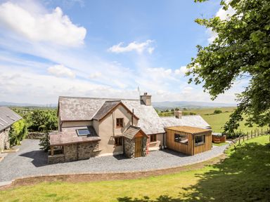 A country house with a stone and plaster exterior and a wooden extension surrounded by fields and trees at Hafotty Gelynen Maerdy near Corwen