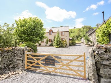 A gravel driveway with a wooden gate leading to a two-story house and stone buildings at Hafotty Gelynen in Maerdy near Corwen