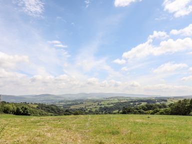 A grassy field with trees and hills in the distance under a partly cloudy sky at Hafotty Gelynen in Maerdy near Corwen