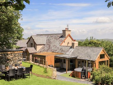 A patio with a dining table and chairs next to a house with slate roofs and a hot tub in the garden at Hafotty Gelynen in Maerdy near Corwen