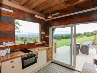 A kitchen with wooden counters a stove toaster kettle a window and sliding glass door opening to a deck with outdoor chairs at Woodland Pod Maerdy near Corwen