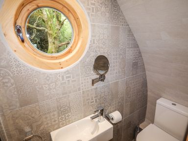 A small bathroom with a round window a white sink a toilet and patterned wall tiles at Woodland Pod in Maerdy near Corwen