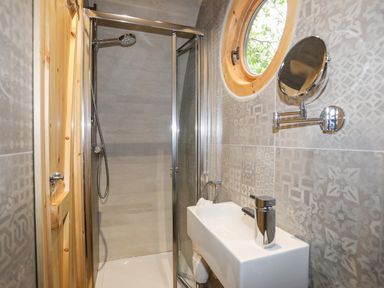A small bathroom with a shower cubicle a white sink and a round window at Woodland Pod in Maerdy near Corwen