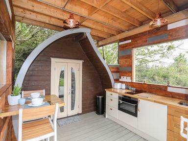 A kitchen area with wooden countertops stools and a dining table with dishes at Woodland Pod Maerdy near Corwen