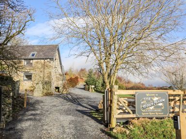 A gravel driveway leading to a stone building with a wooden gate and a sign for The Hidden Meadow at Hafotty Gelynen rural retreat