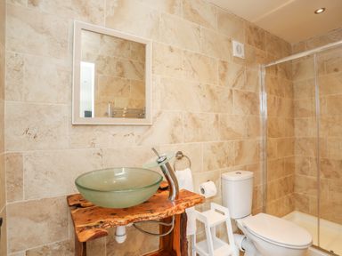 A bathroom with a glass bowl sink on a wooden counter a toilet a small white step stool and a shower at Meadow Lodge in Maerdy near Corwen