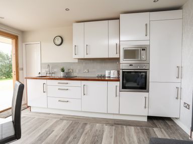A kitchen with white cabinets a wooden countertop a microwave an oven and a black chair at Meadow Lodge in Maerdy near Corwen