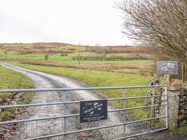 A metal gate with signs leading to a gravel road and grassy fields with hills in the background at Hidden Meadow in Maerdy near Corwen