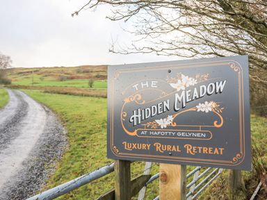 A sign for The Hidden Meadow luxury rural retreat next to a gravel driveway and green fields at Meadow Lodge in Maerdy near Corwen