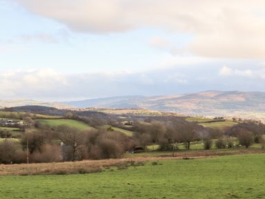 A landscape with fields trees and hills under a partly cloudy sky at Meadow Lodge Maerdy near Corwen