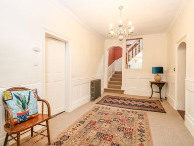 A hallway with stairs rugs a wooden chair with a cushion a small table with a lamp and a chandelier at Enterprise House in Bury St Edmunds