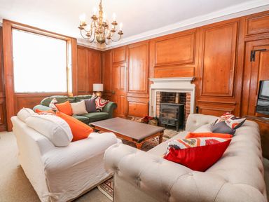 A living room with wooden paneling a chandelier sofas with cushions a coffee table and a fireplace at Enterprise House in Bury St Edmunds