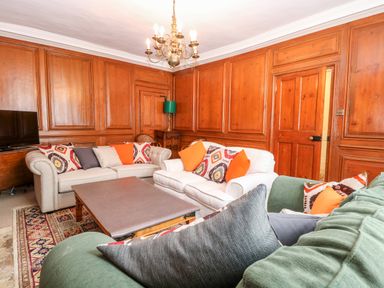 A living room with wooden panel walls sofas with cushions a chandelier and a TV at Enterprise House in Bury St Edmunds
